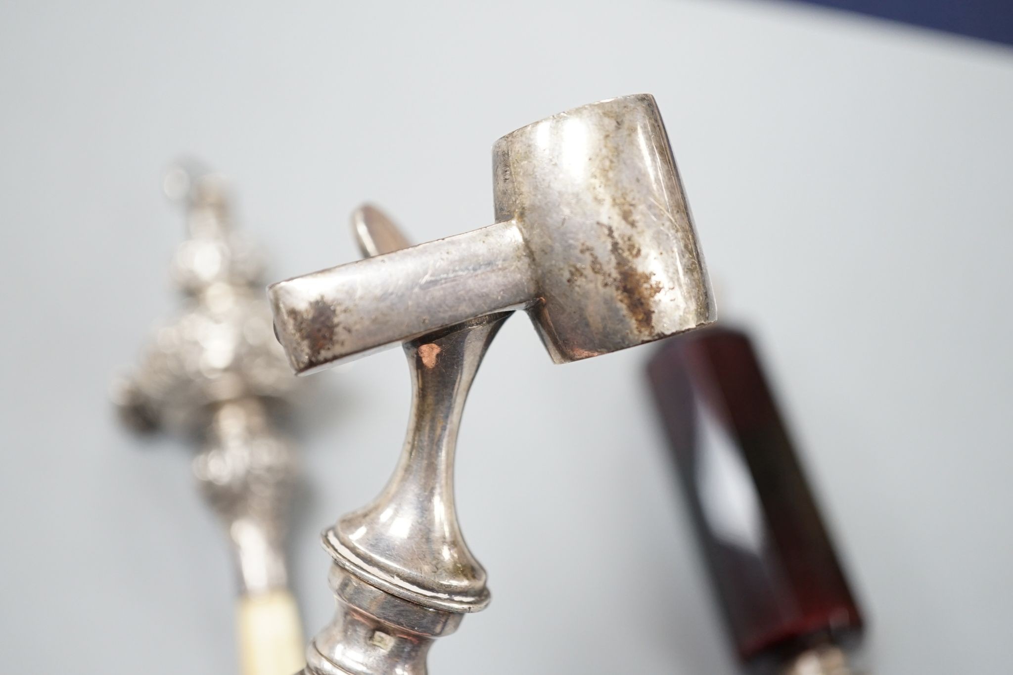 A silver mounted rattle, a white metal mounted double ended ruby glass cent bottle and a silver plated handled roast joint holder.